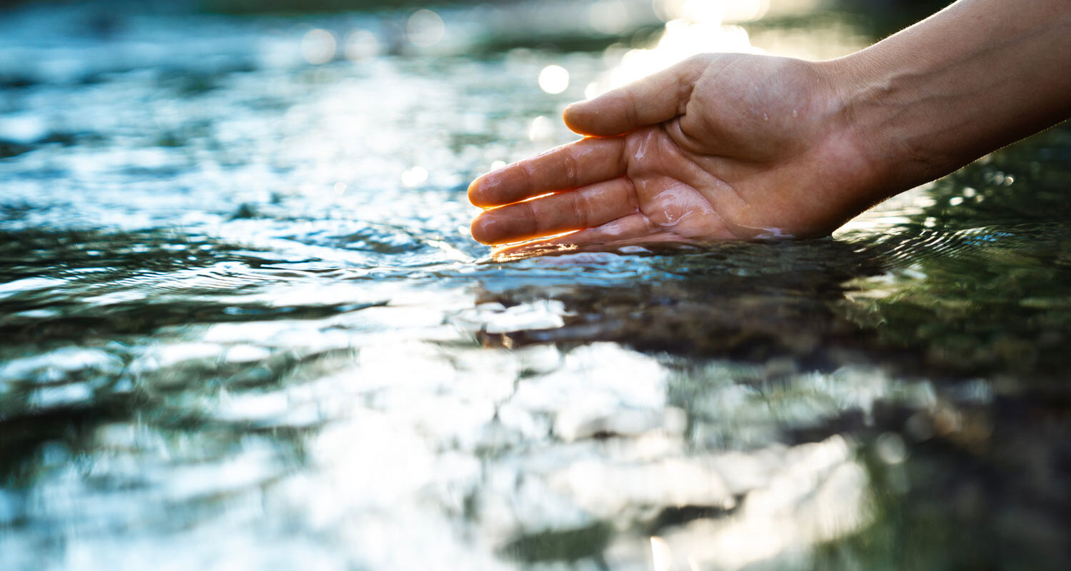 Een vrouw gaat met haar hand door het water van een rivier. Waterzuivering is van cruciaal belang om de beschikbaarheid van schoon water te waarborgen en milieuvervuiling tegen te gaan.