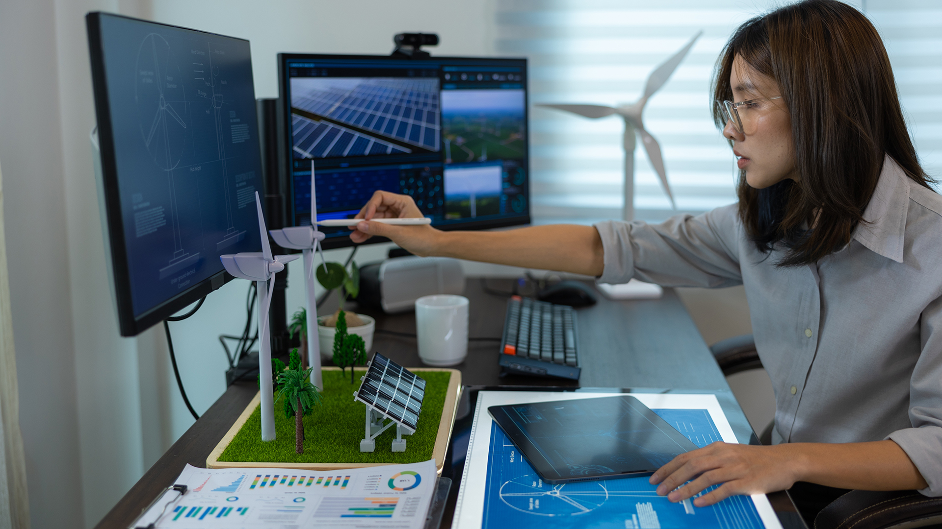 female engineer working on a computer surrounded by miniature energy objects like solar panels