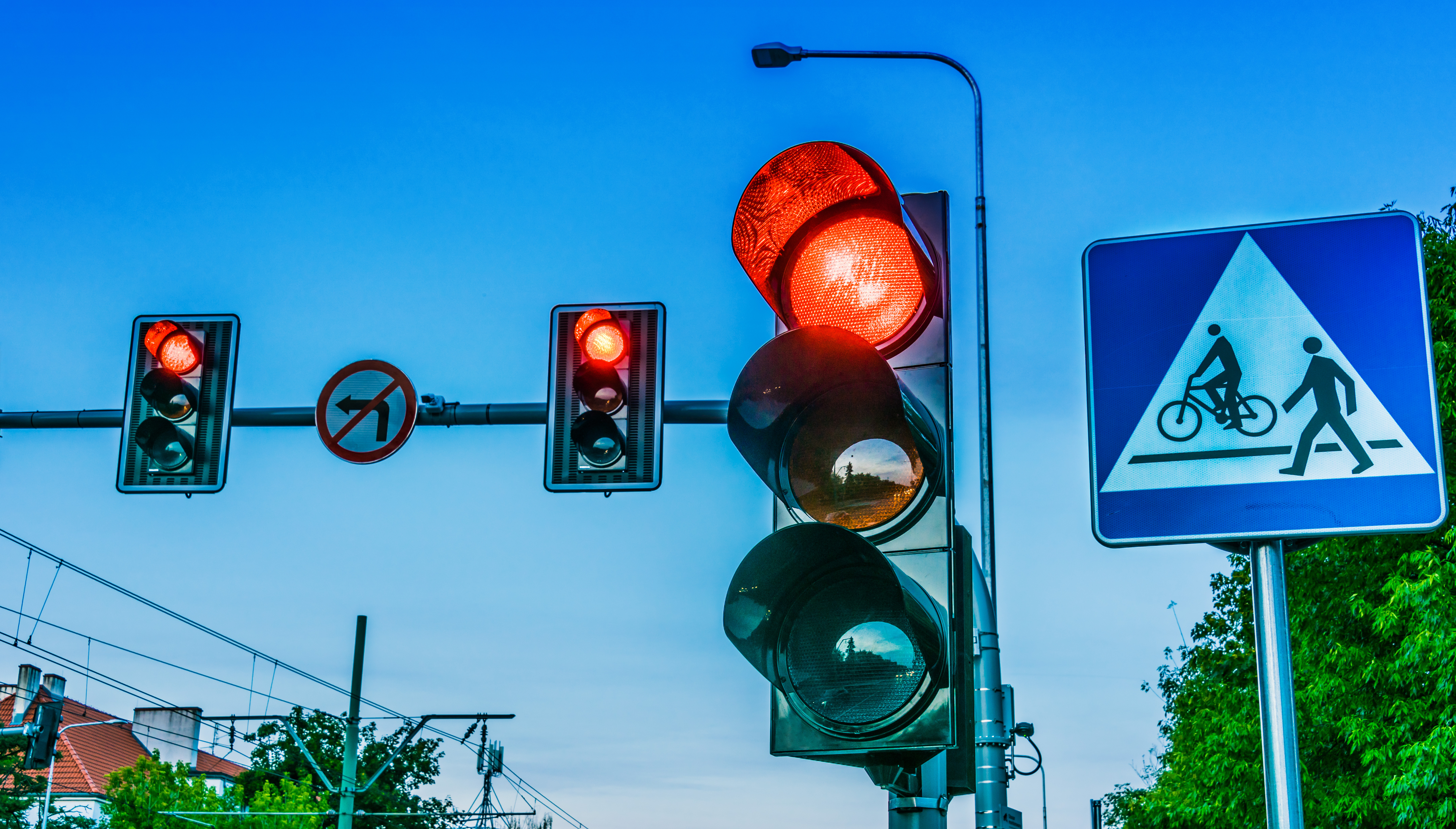 Verkeerslichten boven een kruispunt in de stad. Een verkeersbord met een voetganger en een fiets.