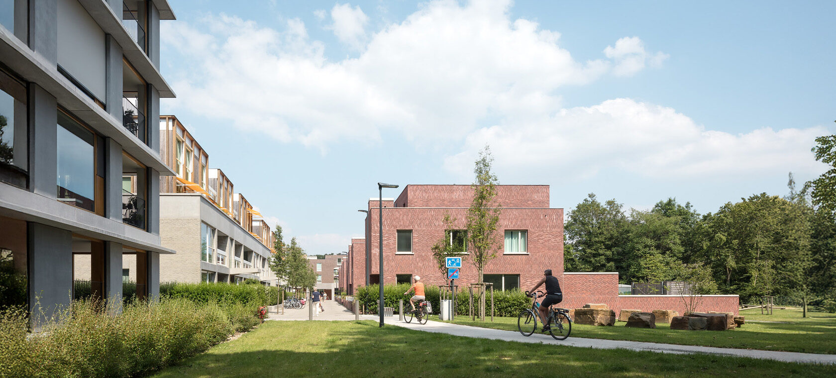 open ruimte met woningeenheden, in het groen met 2 personen op een fiets