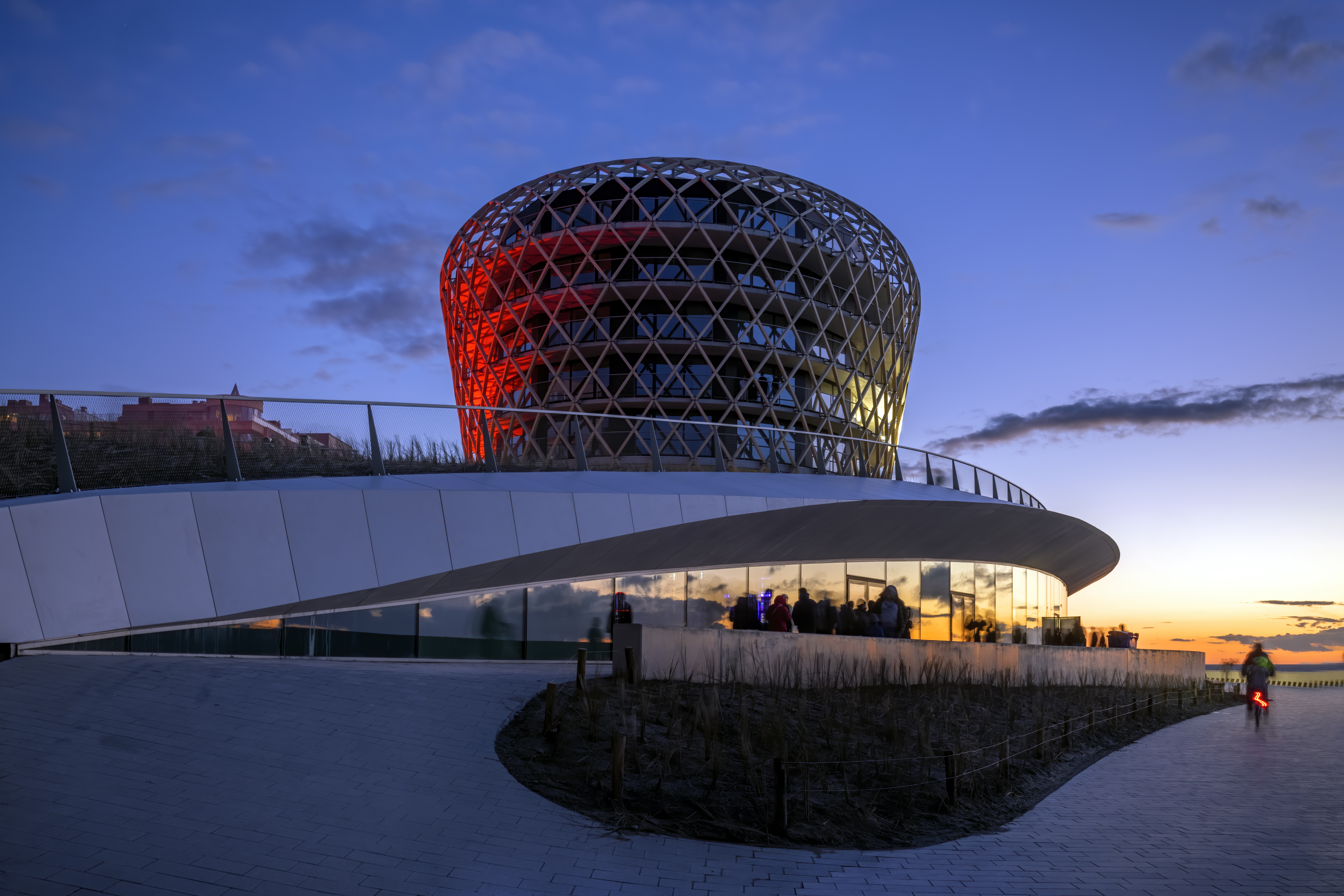 exterior photo of SILT, a mixed-use project in Middelkerke with casino, hotel, restaurant and event hall, illuminated by the last light of sunset and with a red glow of the lighting design