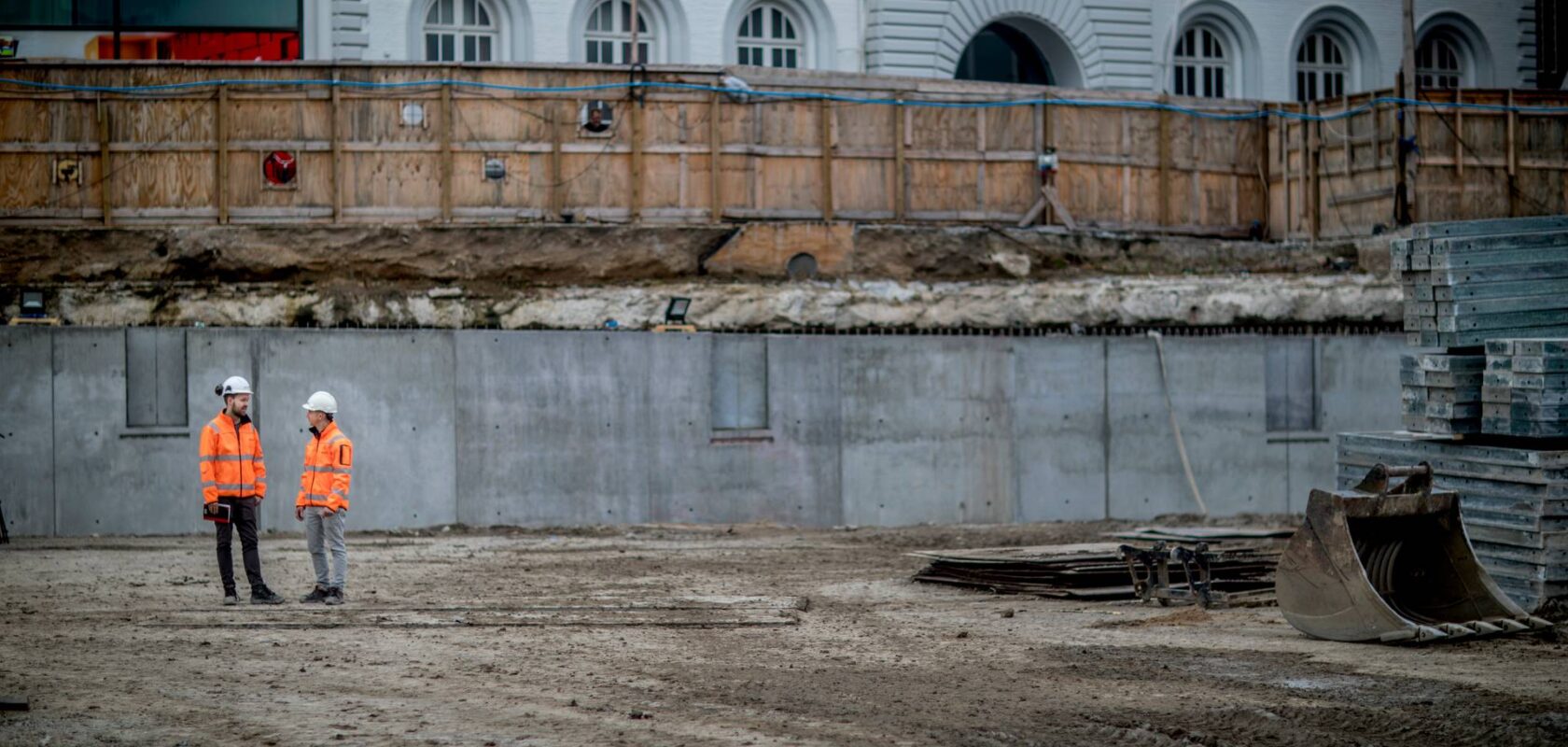 photo of an excavation site for a building project, with two Sweco workers in safety gear
